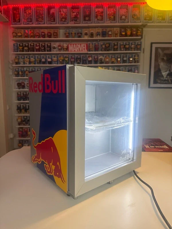 Mini nevera encendida sobre una mesa junto a una estantería de figuras